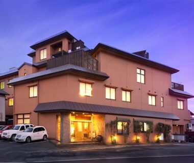 Lit multi-story ryokan exterior with entrance and parked cars at dusk, Ryokan Kawana, Chiba, Kantō