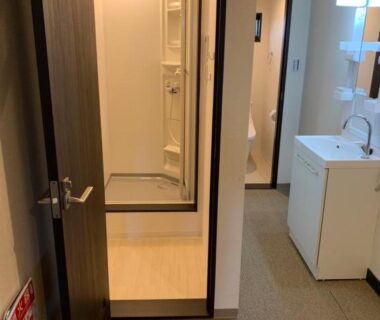 Corridor leading to compact bathroom with shower stall and washbasin at Mei Wa Inn Kyoto