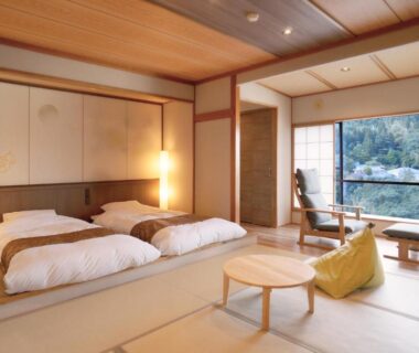 Tatami room with futon beds, shoji screens, low table and window overlooking wooded valley at Tsukioka Onsen, Niigata