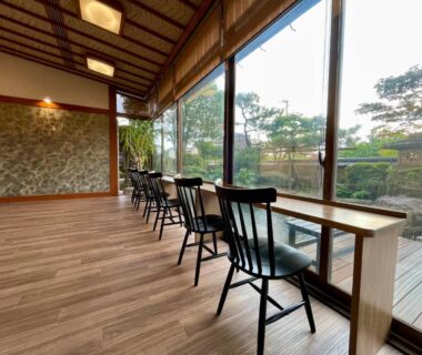 Long wooden counter and chairs facing garden through large glass windows in ryokan common seating area