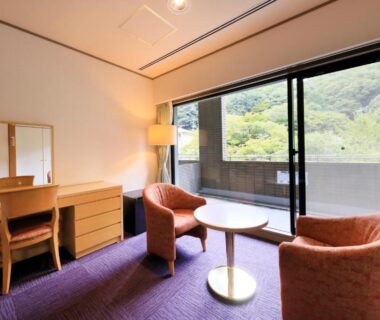 Seating with two armchairs, round table and dressing desk opening to balcony with green hillside view in Arima Onsen, Hyōgo