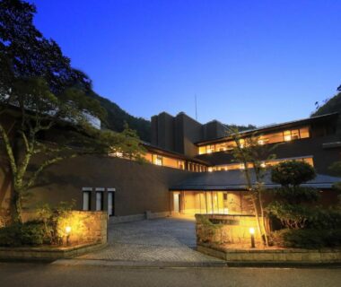 Exterior of La Conte Arima with lit entrance, driveway and surrounding trees against twilight sky in Hyōgo