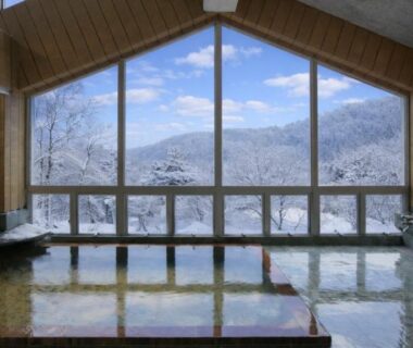 Spacious indoor onsen bath with large windows overlooking snow-covered mountains in Nagano