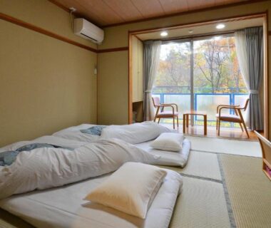 Tatami room with futons, low table and balcony view of trees at Matsutake Sansō in Nagano