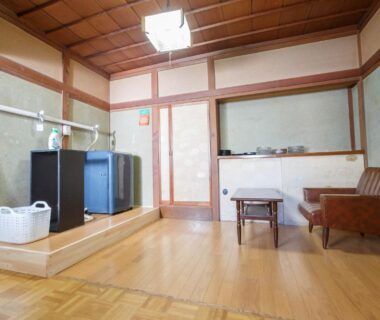 Wooden floored interior with low table, shoji screens, small fridge and seating at Ryokan Kashiwaya Nagano