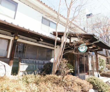 Wooden facade and entrance with shrubs at Ryokan Kashiwaya share house et guest house in Nagano Chūbu