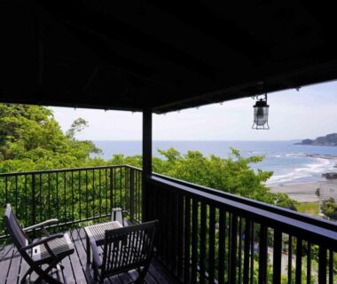 Wooden balcony with chairs and table overlooking sea, beach and greenery at Kiri no Kaori Sakura, Shizuoka