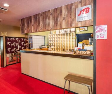 Hotel reception counter with wooden paneling, red carpet, key cubbies and a small stool at Kitakaruizawa Kogen Hotel, Gunma