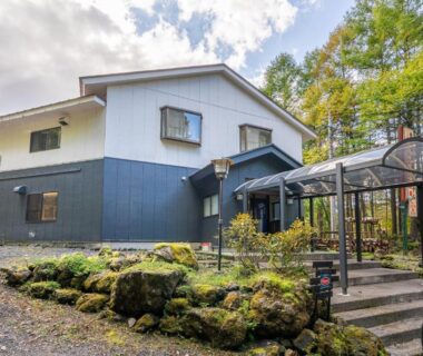 Two-story ryokan building with glass entrance canopy, mossy stone garden and forested surroundings at Kitakaruizawa Kogen Hotel, Gunma