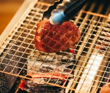 Slices of meat grilling on wire mesh over charcoal with tongs in ryokan dining setting Hokkaidō