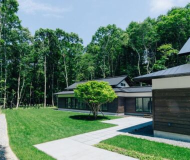 Grassy courtyard, paved paths and wooden ryokan buildings with forest backdrop at 森のオーベルジュ 三 みつ Hokkaidō