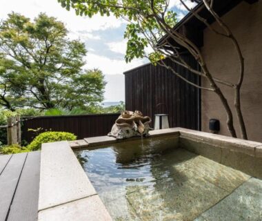 Outdoor stone soaking tub with wooden deck and garden at Musōan Biwa, Shizuoka