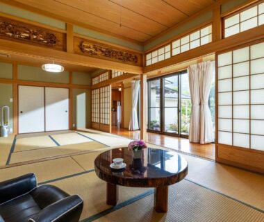 Spacious tatami room with low round table, shoji screens, armchairs and garden-facing sliding doors at Rakushinkan Oita
