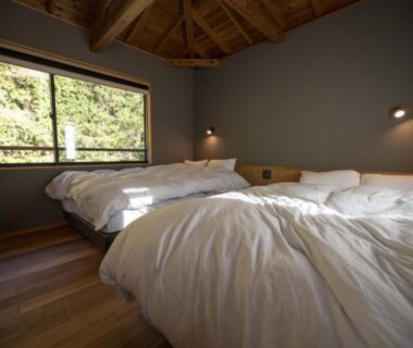 Two beds on wooden floor under vaulted ceiling with window revealing forest view at Yudono Totonoyu Shizuoka