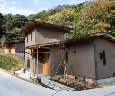 Cluster of earthy ryokan buildings with wooden doors along a hillside path in Shizuoka