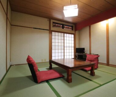 Tatami room with low wooden table, red floor chairs, shoji sliding doors and compact TV at Minshuku Hiroshige, Ōita