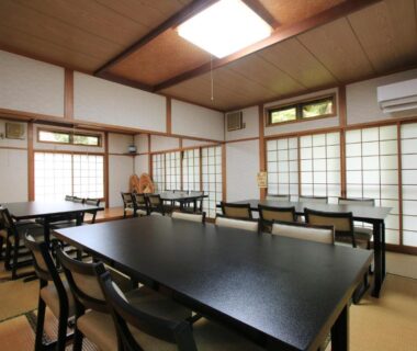 Tatami dining area with low black tables, chairs and shoji screens at Minshuku Hiroshige in Ōita