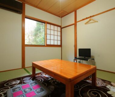 Traditional tatami room with low wooden table, cushions, shoji window and small TV at Minshuku Hiroshige in Ōita, Kyūshū