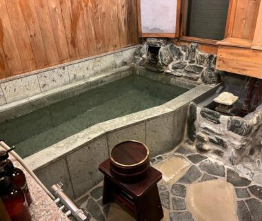 Small indoor bath with stone floor, wooden walls, stools and buckets at Atasawaya Ryokkan