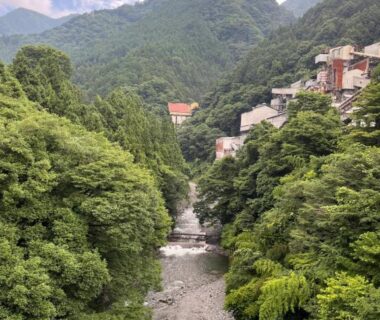 River gorge with rocky bed and lush green hillsides, buildings near Atasawaya Ryokkan in Tokyo Kantō