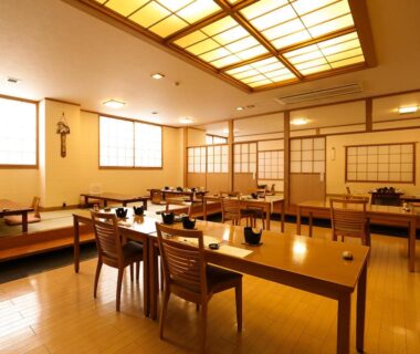 Spacious ryokan dining room with low wooden tables, chairs, shoji screens and table settings in Shizuoka