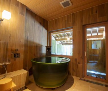 Indoor wooden bathing room with round green tub, shower and small stool at Senshin Waho in Hyōgo, Kansai