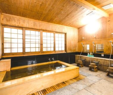 Traditional wooden indoor onsen with soaking tub, washing stations, shoji window and stone floor at Shojo Shin-in Wakayama