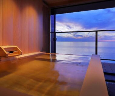 Indoor wooden bath overlooking the sea at dusk at Yūsuitei Isagoya in Yamagata