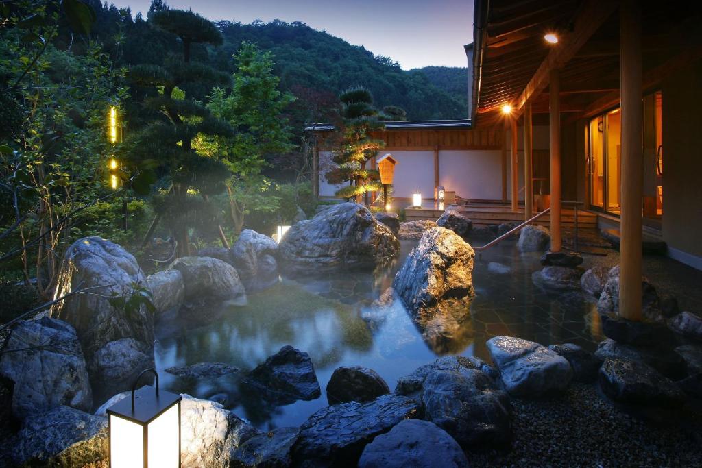 Outdoor rock onsen Yūsen Shidate Iwate Stone-lined outdoor hot spring with wooden veranda, lanterns, and mountain backdrop at Yūsen Shidate, Iwate, Tōhoku