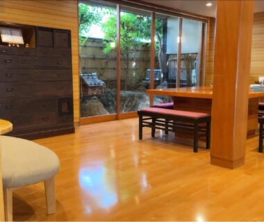 Polished wooden lounge with low table, benches and glass doors opening onto a small courtyard garden in Hyōgo