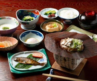 Assorted Japanese breakfast with grilled fish, rice, soup, and pickles on wooden table at Yushō Fukujikan