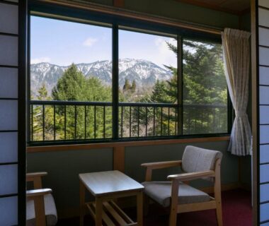 Tatami room seating by window with mountain and forest view at Yushō Fukujikan in Gifu