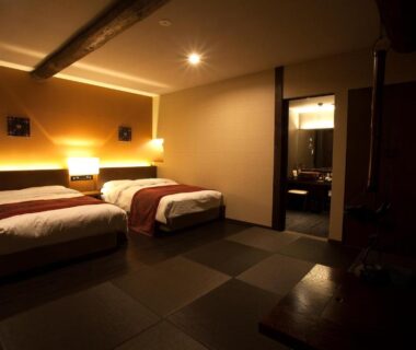 Warm lit tatami twin room with two beds and wooden beams at Oyado Kotobuki Yumura Onsen Hyōgo