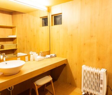 Bright wooden wash area with round basin, mirror, stool and heater at Yune no Sakura in Gunma