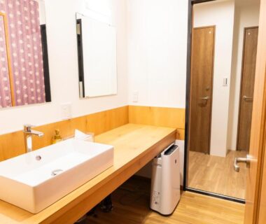 Vessel sink on wooden counter with mirror, patterned curtain and wooden door at Yune no Sakura in Gunma