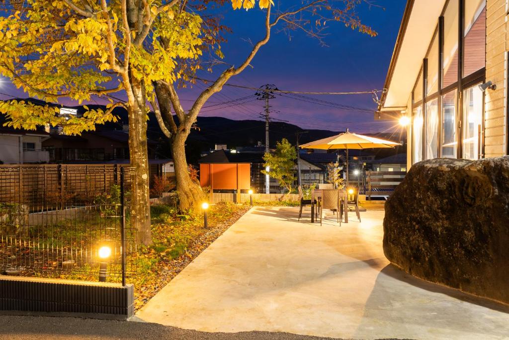 Evening terrace at Yune no Sakura Gunma Exterior terrace with lit pathway, outdoor seating and umbrella beside glass-walled ryokan building in Gunma