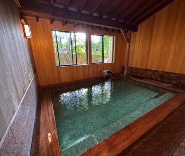 Indoor wooden onsen bath with stone edging and window view at Fukunoya, Gunma, Kantō
