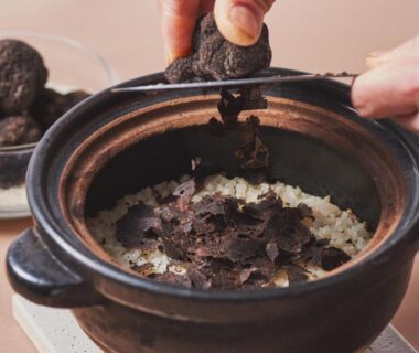 Hands shaving black truffle over rice in clay pot at 源泉掛け流しの宿Albergo湯楽, Kanagawa, Japan