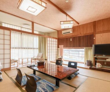 Tatami room with low lacquer table, zabuton cushions, stacked futons and shoji screens at Shōgetsu, Atami