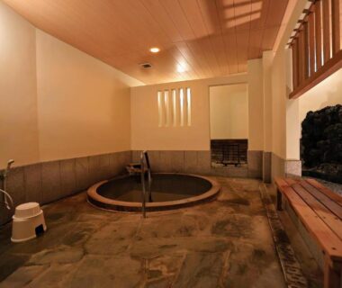 Round wooden indoor onsen with stone floor, washing stools and bench at Ryokan Hōetsu in Atami