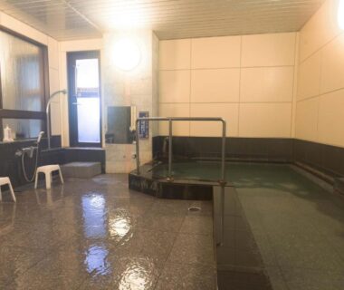 Tiled indoor onsen bath with shower stools, handrail and small windows at Yunoyado Hiratsuru, Atami Onsen