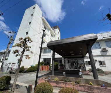 Multi-story white building with covered entrance and trimmed shrubs, Keyaki no Yado, Yamagata, Tōhoku, Japan