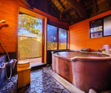 Enclosed wooden soaking tub with shower, stone floor and small garden view at Ryoso Makibanoie, Ōita, Kyūshū