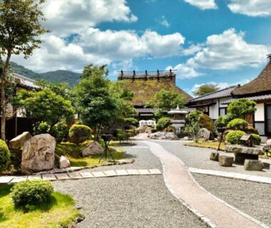 Thatched-roof courtyard with stone path and manicured garden at Ryoso Makibanoie, Ōita, Kyūshū