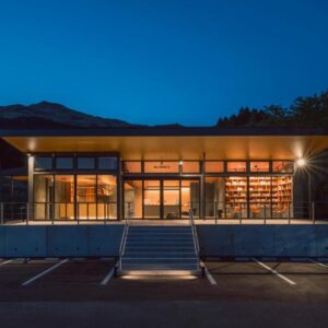 Lit glass facade and steps at Takenokura Sansō with parking and mountain silhouette in Kumamoto, Kyūshū