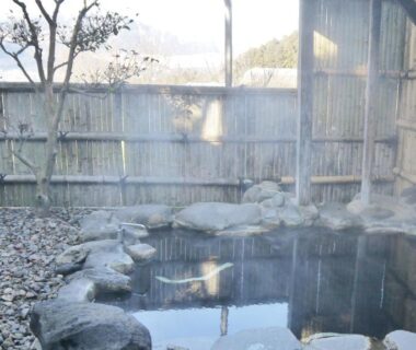 Outdoor stone onsen bath with steam, bamboo fence and pebble courtyard at Takenokura Sansō in Kumamoto