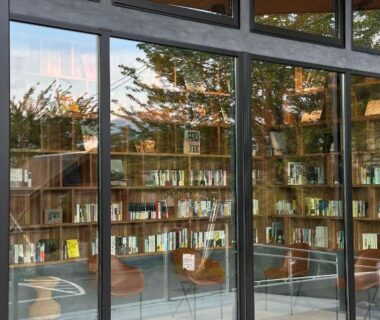 Floor-to-ceiling glass library with wooden bookshelves and seating overlooking trees at Takenokura Sansō, Hakusui Onsen, Kumamoto