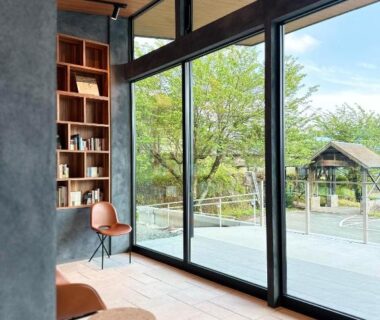 Glass windows reveal terrace and green garden, bookshelves and seating at Takenokura Sansō in Kumamoto, Kyūshū