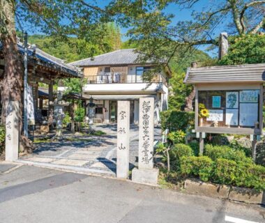 Stone gate and entrance path to Kiimiso ryokan with traditional wooden building and garden in Wakayama