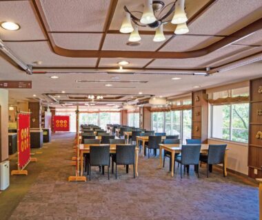 Spacious ryokan dining area with tables, chairs, carpet and large windows overlooking greenery at Kiimiso, Wakayama